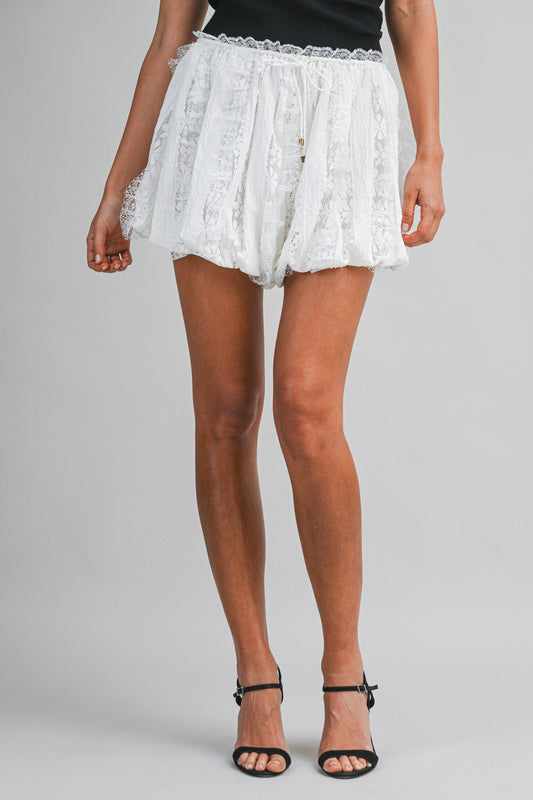 White lace shorts worn by a person on a gray background