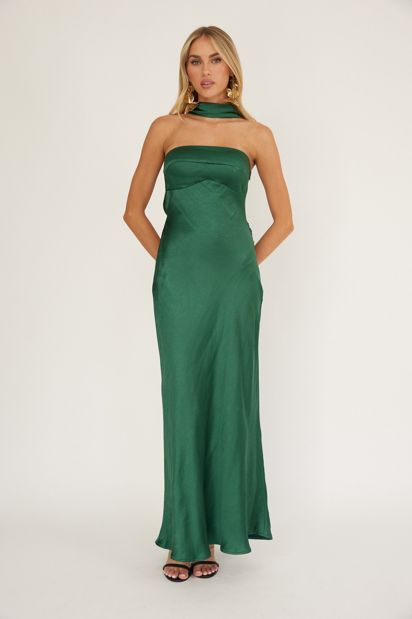 Woman wearing green satin halter neck floor-length gown with scarf tie detail.