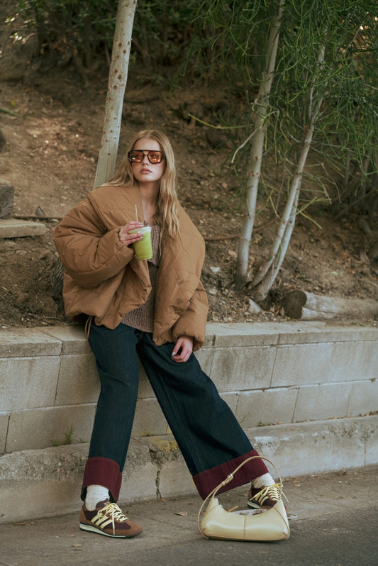 Woman in a brown jacket and green pants sitting on stone steps outdoors.
