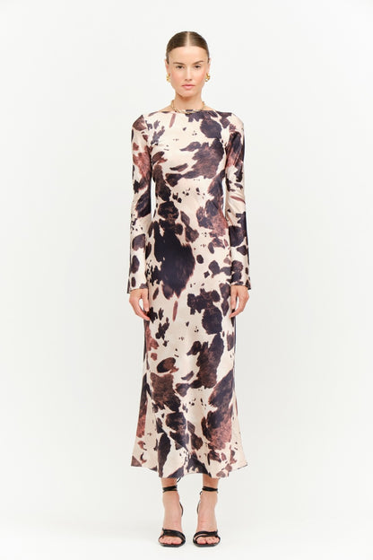 Model wearing the Georgie Cow Dress, a long-sleeve satin cow-print maxi dress.
