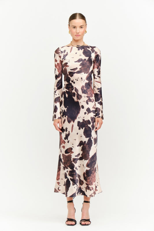 Model wearing the Georgie Cow Dress, a long-sleeve satin cow-print maxi dress.