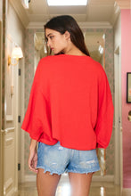 Load image into Gallery viewer, Woman wearing a red top and denim shorts in a hallway.