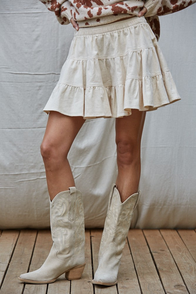 Woman wearing the High Noon Tiered Mini Skirt in cream cotton corduroy with tiered flared design and elastic waistband.