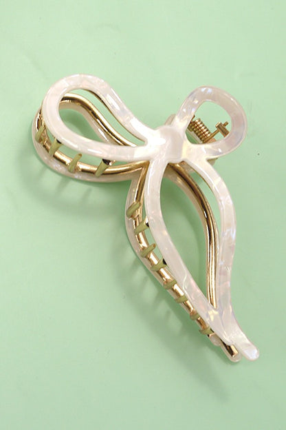Gold and white bow-shaped hair clip on a light green background