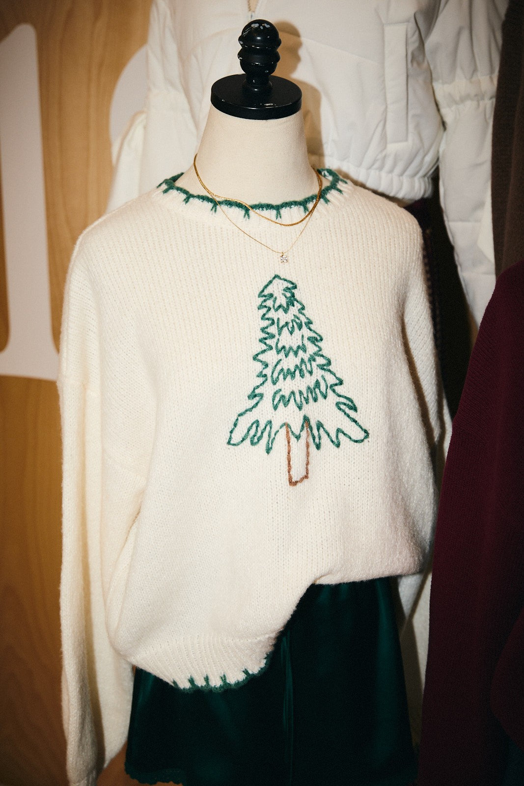 Model wearing cream oversized sweater with stitched Christmas tree design and green trim