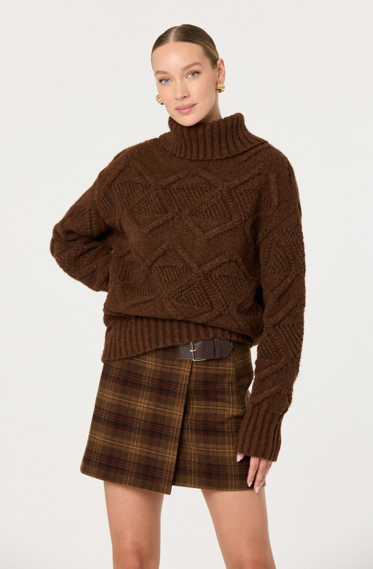 Woman wearing a brown cable knit sweater and plaid skirt on a white background