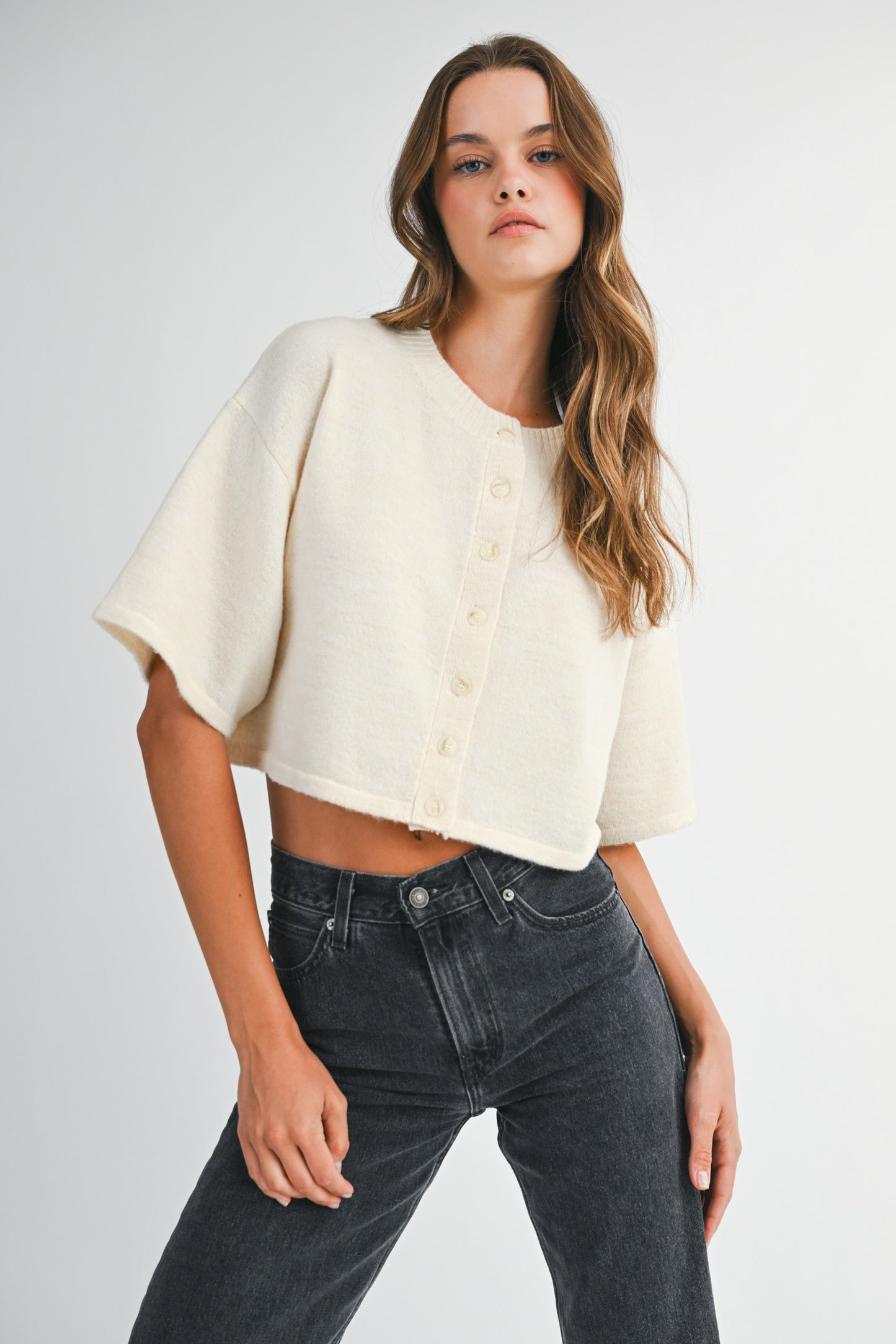 woman wearing cream cropped knit cardigan with elbow sleeves and black jeans