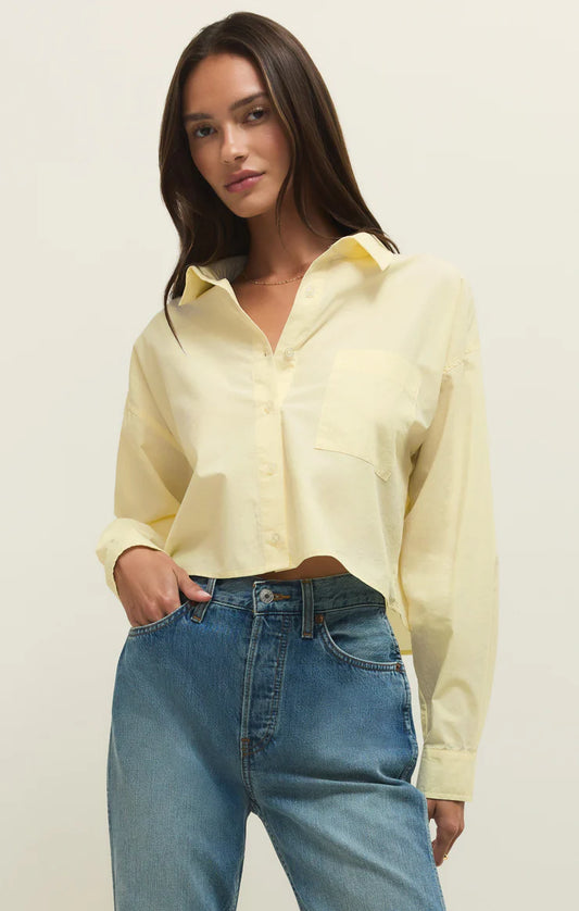 Woman wearing a light yellow blouse and blue jeans against a plain background