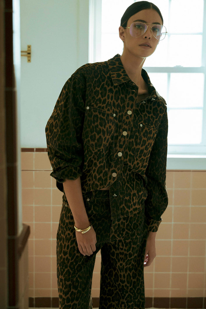 Model wearing a leopard print button-down denim jacket with matching pants in a neutral tiled room