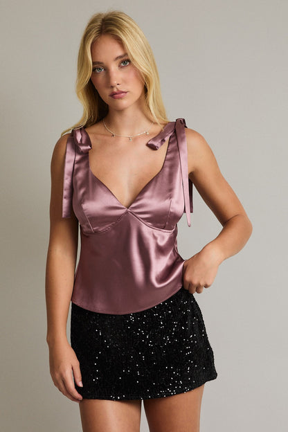 Model wearing mauve satin V-neck top with bow-tie shoulder straps and black sequin skirt