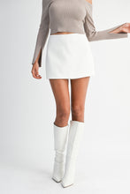 Load image into Gallery viewer, Model wearing a high-waist white mini skort styled with a taupe off-shoulder top and knee-high white boots