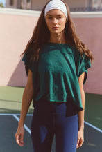 Load image into Gallery viewer, Woman wearing a green top and blue leggings on a tennis court
