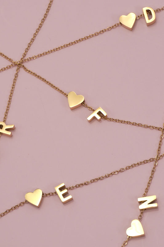 Gold necklaces with letters and heart charms on a pink background