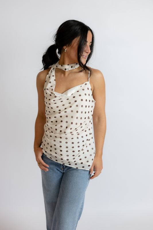 Woman wearing a polka dot halter top and light blue jeans on a white background