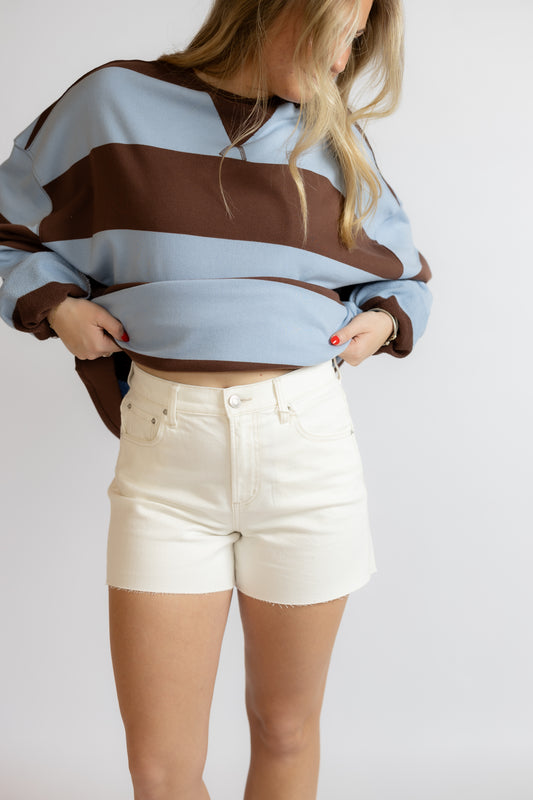 Person wearing a striped sweater and white shorts on a plain background