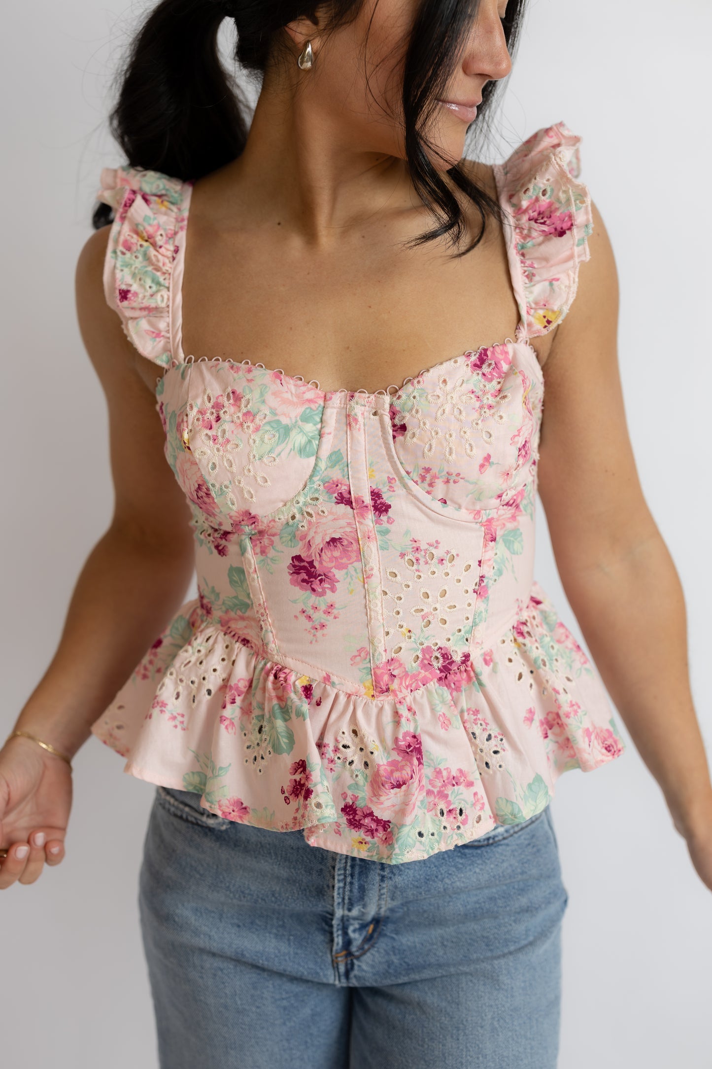 Woman wearing a floral top and jeans against a plain background