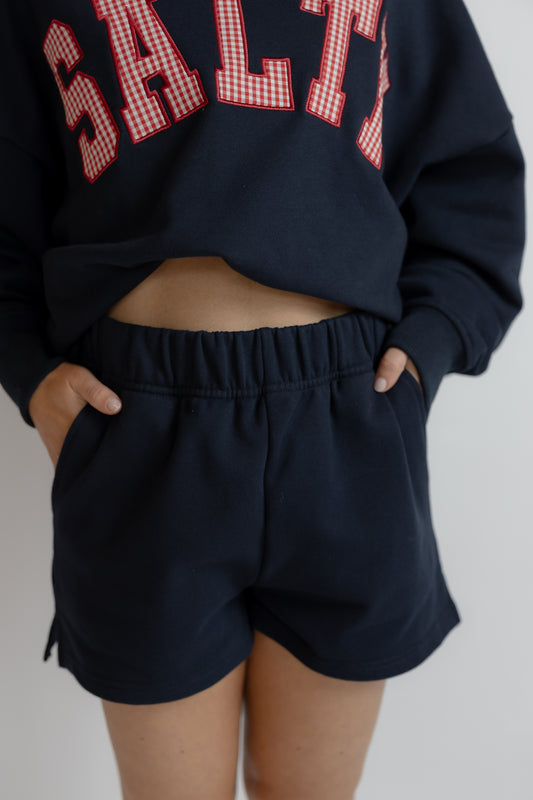 Person wearing a navy sweatshirt with red checkered text and matching shorts on a plain background