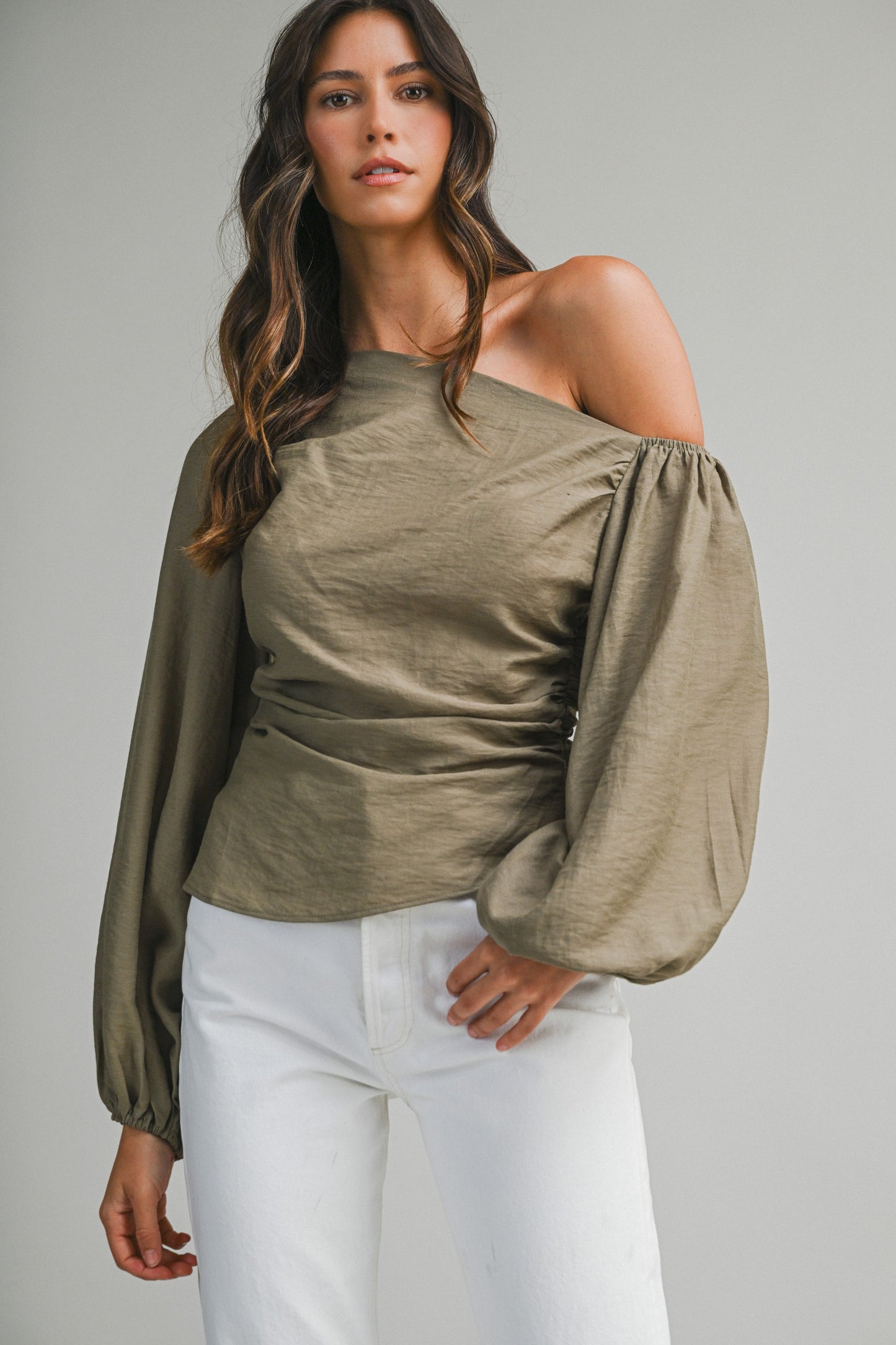 Woman wearing an olive green off-shoulder top with white pants on a gray background