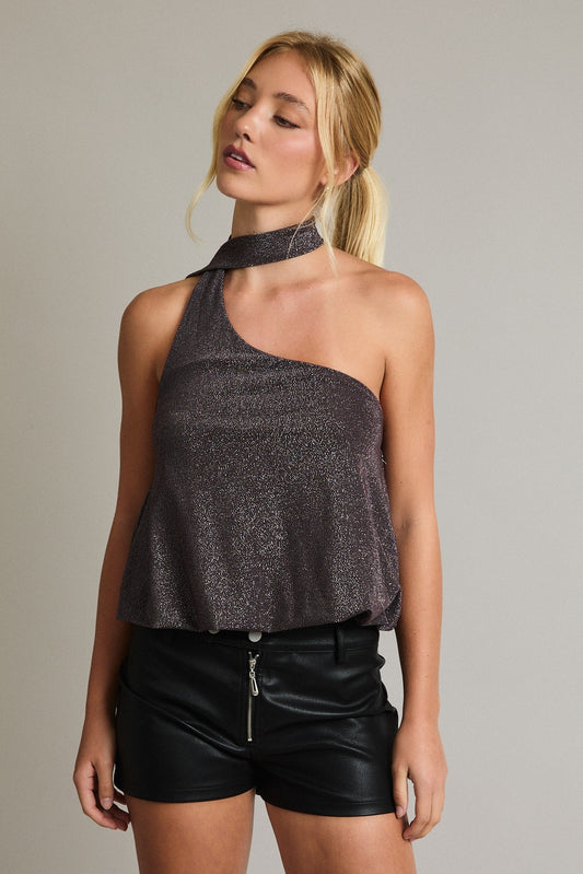 Model wearing metallic one-shoulder top with attached scarf detail and black faux leather shorts