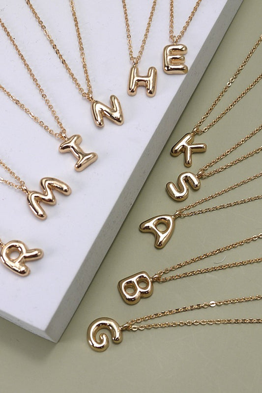 Gold necklaces with letter pendants on a light green background
