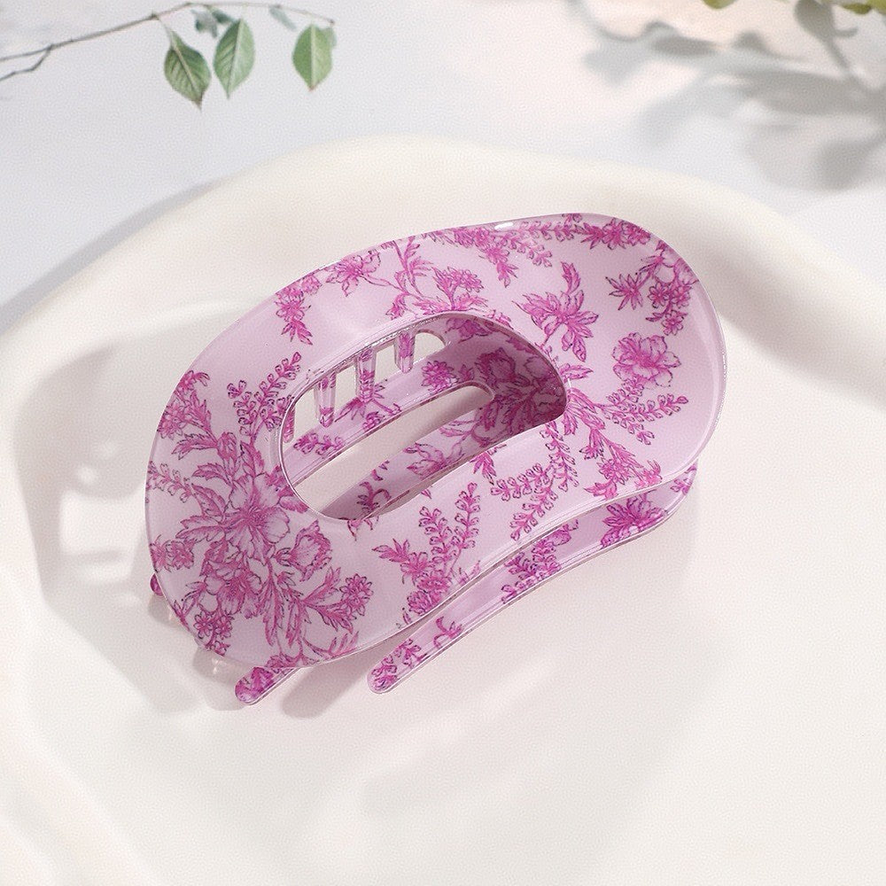 Pink floral-patterned claw clip on a white surface with a light background