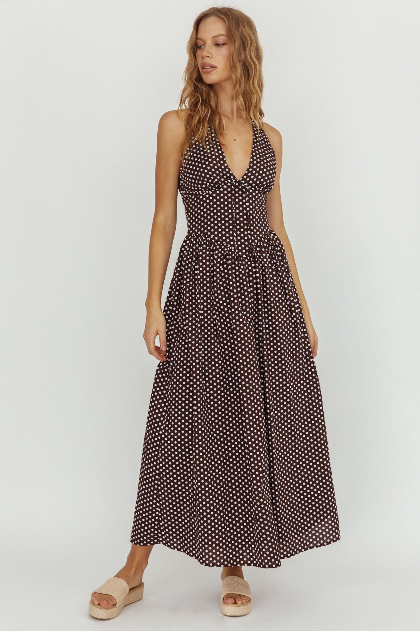 Model wearing Midnight Dot Halter Dress in brown with white polka dots and halter neckline