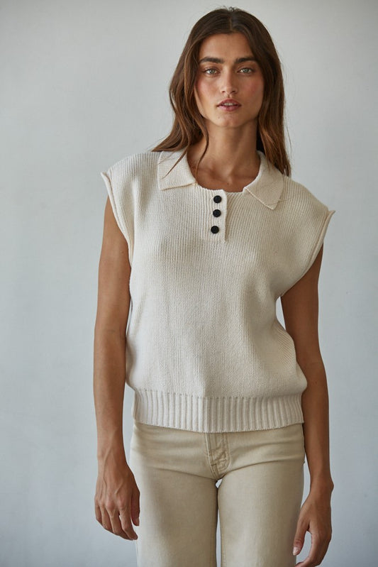 Woman wearing the It’s A Match Polo Vest, a sleeveless ribbed knit polo vest with button-up collar in neutral cream.