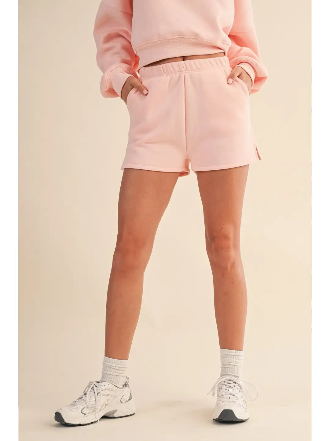 Person wearing a pink sweatshirt and shorts set with white sneakers on a beige background