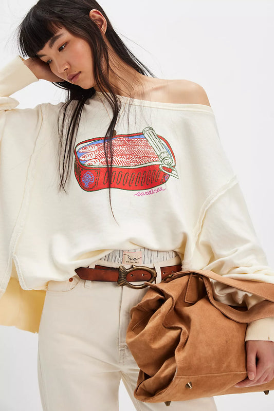 Woman wearing a white off-shoulder sweatshirt with a graphic design, holding a brown bag on a white background