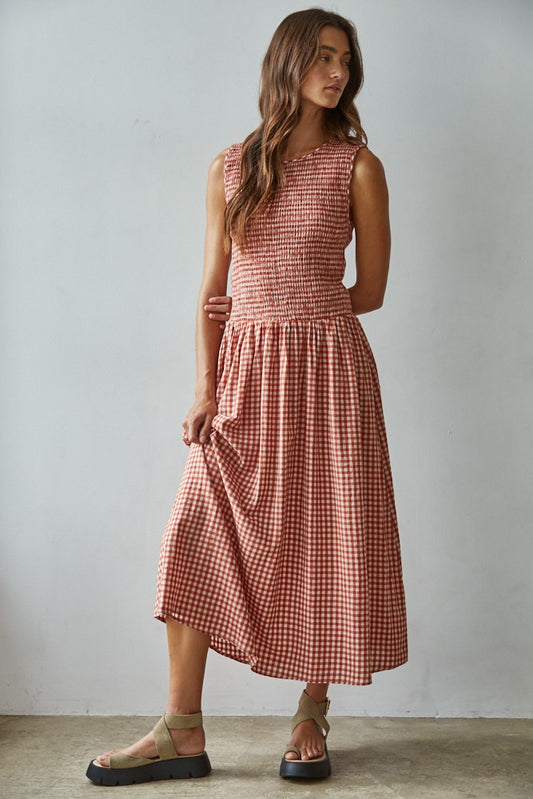 Woman wearing red gingham smocked sleeveless midi dress with flared skirt and sandals.