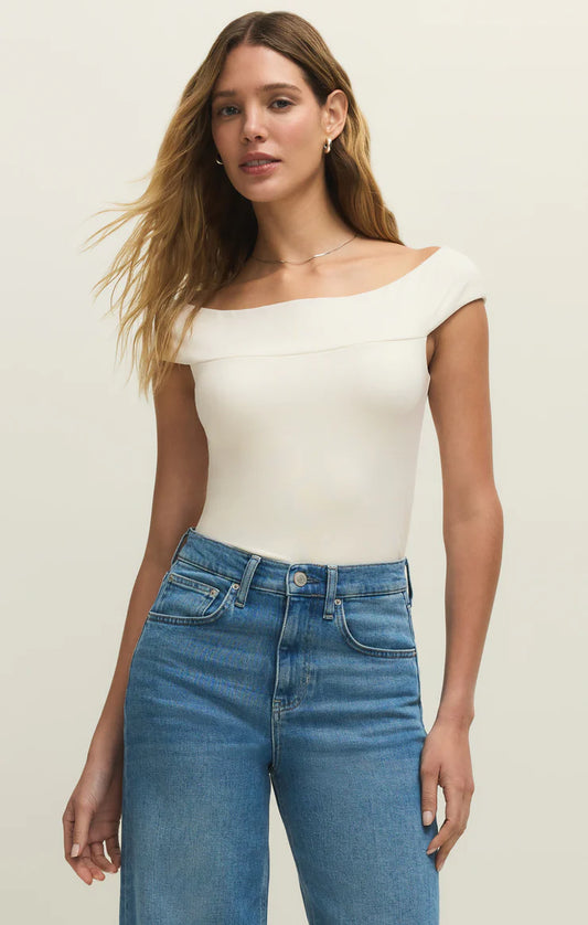 Woman wearing a white off-shoulder top and blue jeans on a plain background