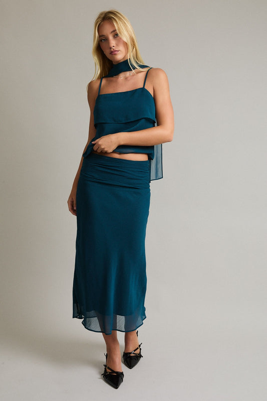 Model wearing teal sleeveless layered top with matching scarf and maxi skirt co-ord set