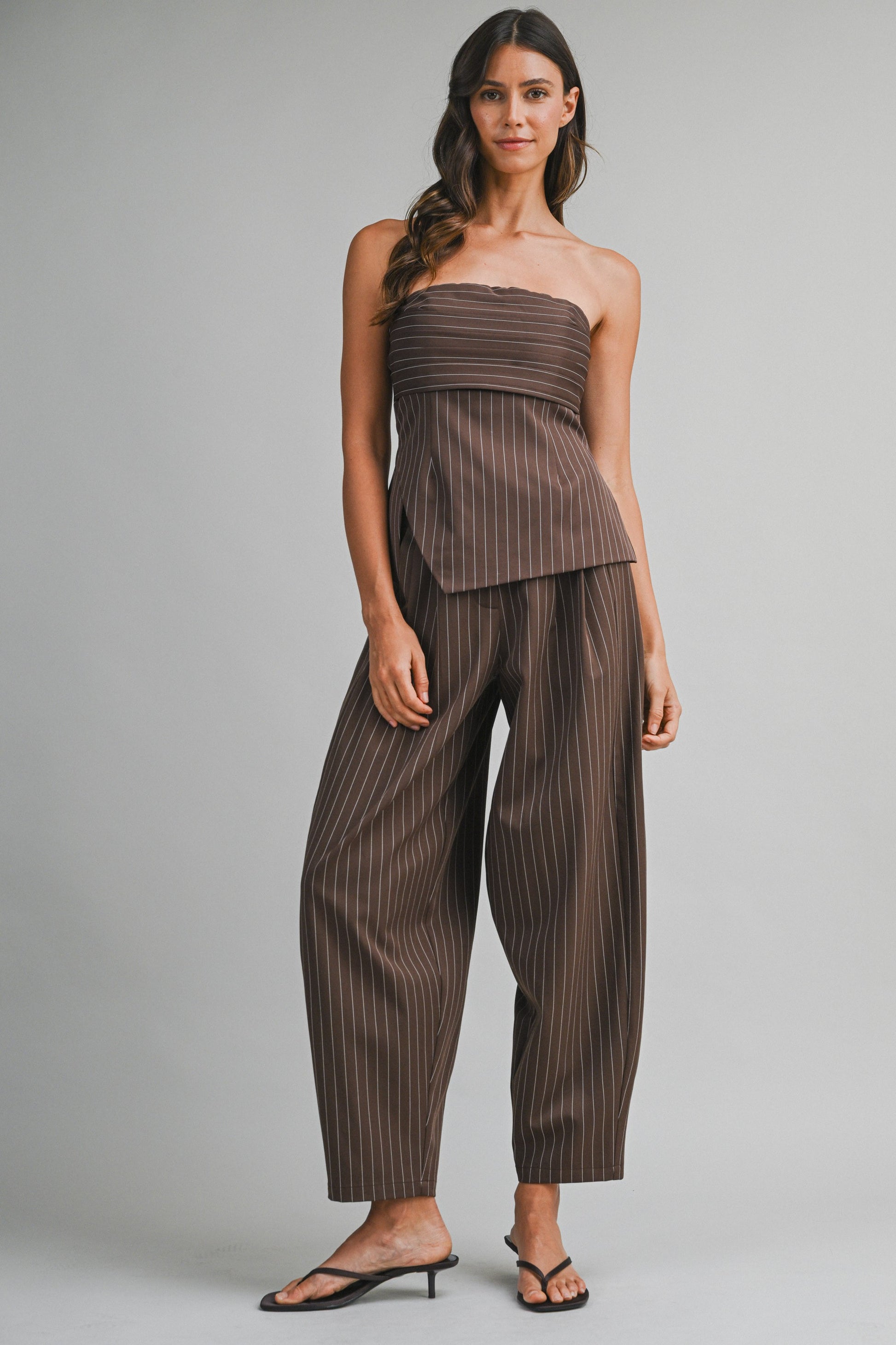 Model wearing a brown pinstripe strapless tube top and cropped barrel-leg trouser set