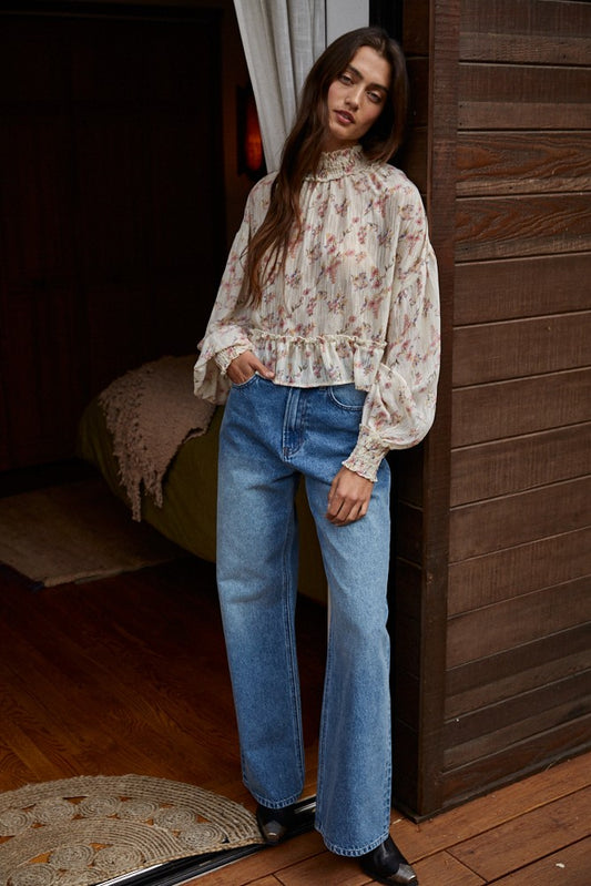 Woman wearing soft floral smocked mock neck blouse with ruffled hem and blue jeans.