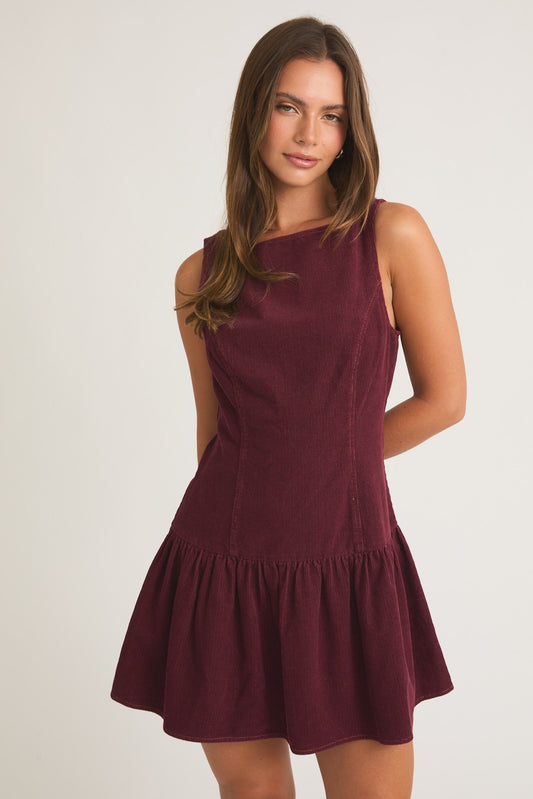 Model wearing burgundy corduroy sleeveless drop-waist mini dress with boat neckline