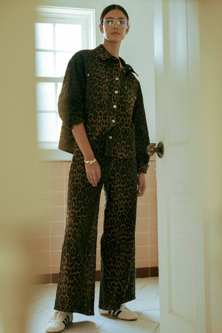 Model wearing leopard print wide-leg jeans with sneakers, standing in a tiled room with natural light